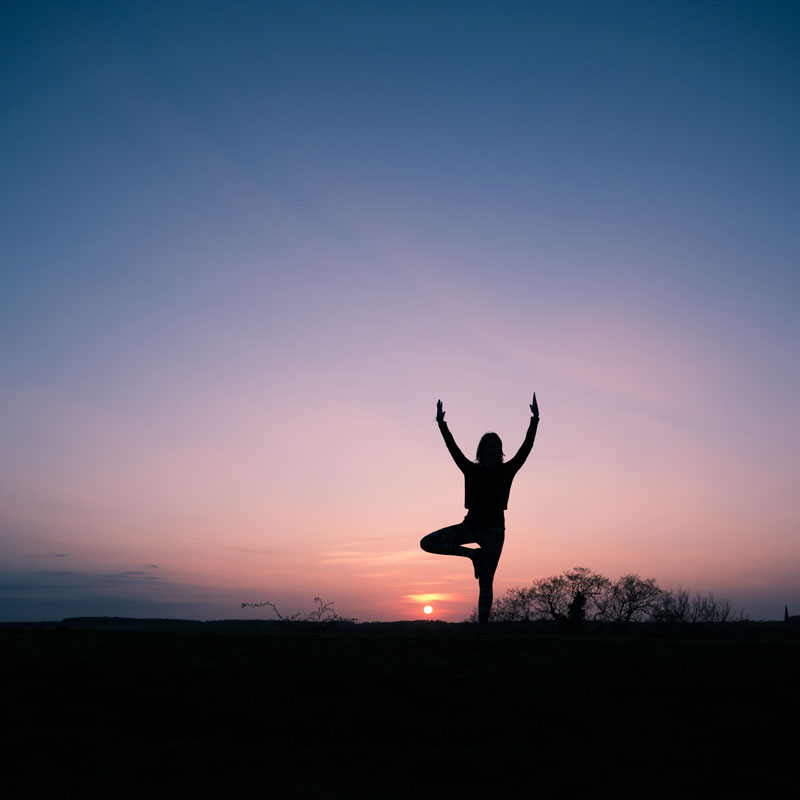 Woman doing yoga in nature at sunset to represent the stress free benefits of GoReady’s VIP Travel Plan