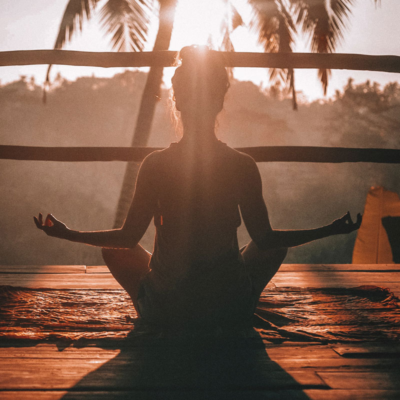 A woman meditating in a tropical setting at sunset who may have purchased a GoReady single-trip plan.
