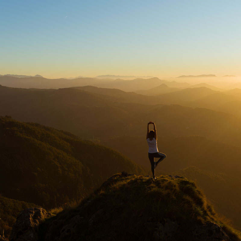 Woman doing yoga on a mountain during sunset while taking one of her multi-trips during the year.