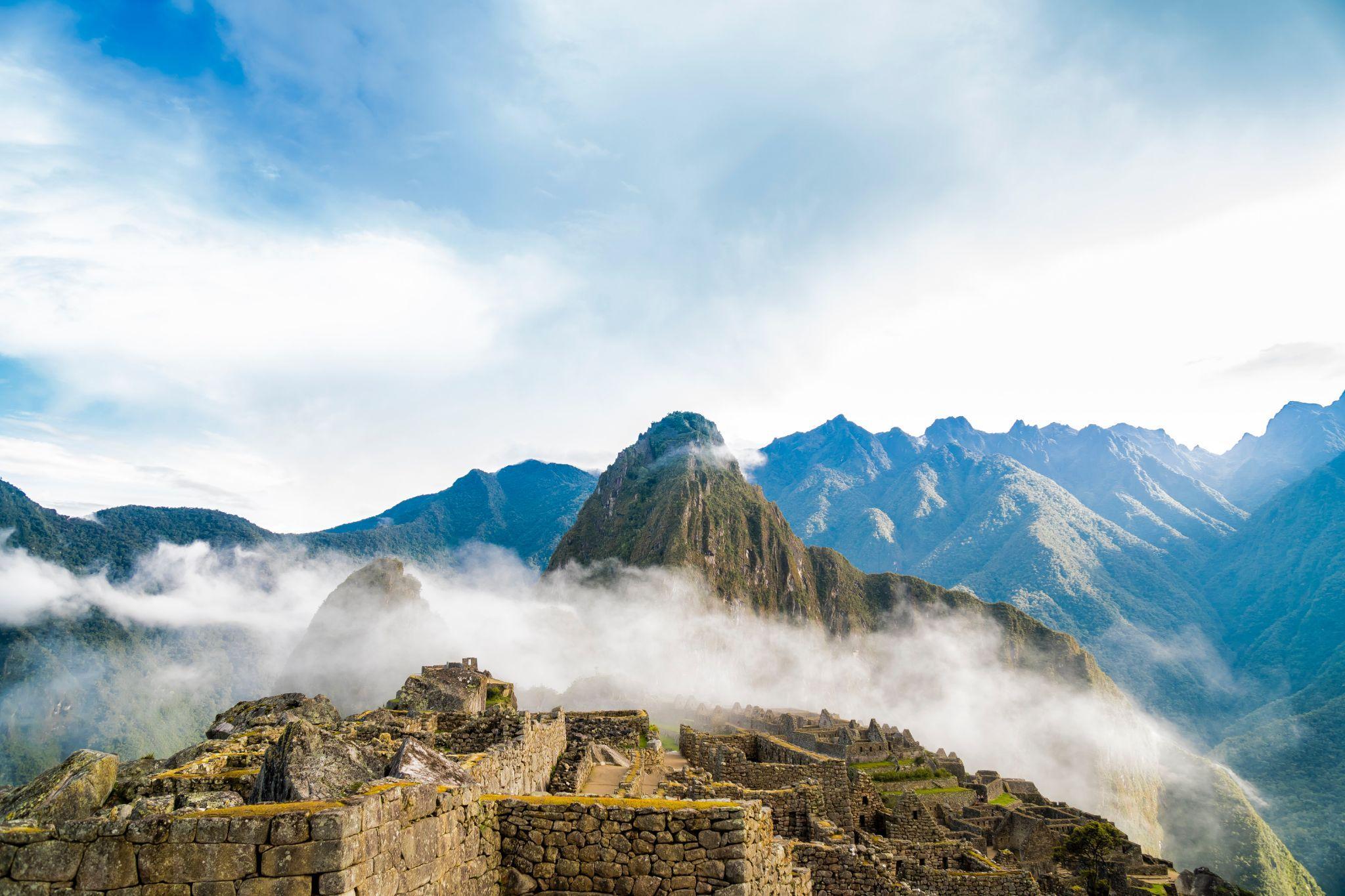 Image of Mach Picchu shrouded in clouds with mountains in the background.
