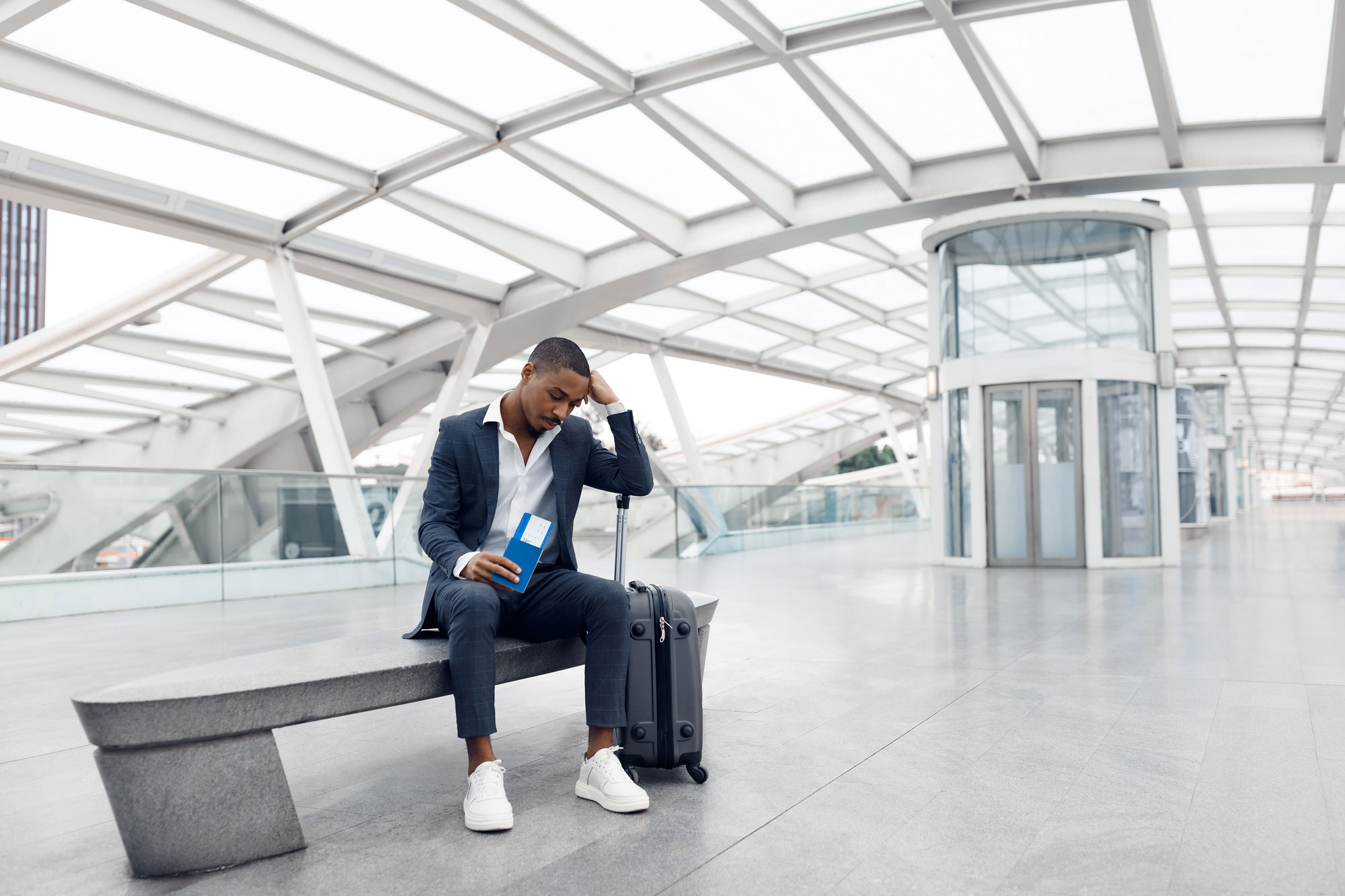 Businessman Sitting With Suitcase At Airport Terminal after a canceled flight who wishes he had purchased travel insurance for flight cancellations.