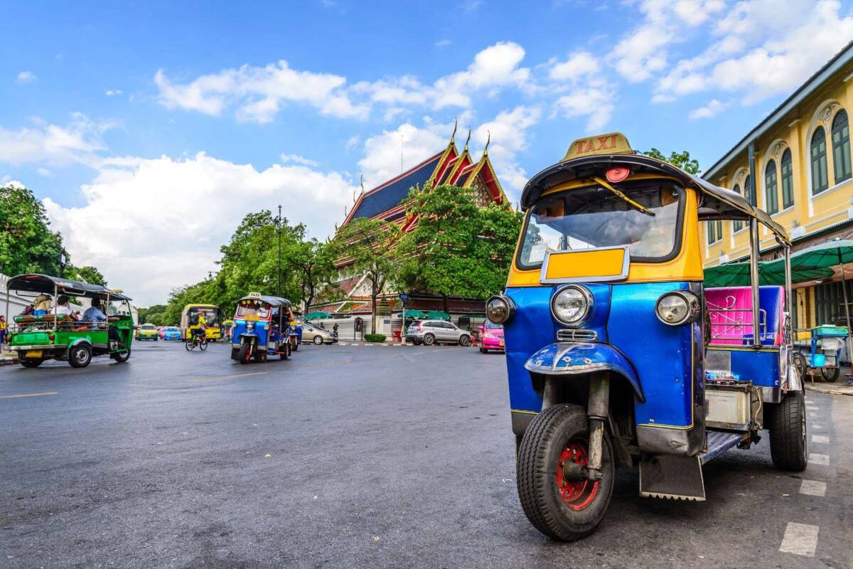 A blue and yellow tuk-tuk, a Thai traditional taxi, stands out on a bustling street in Bangkok.