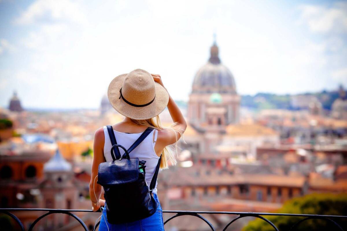 A female traveler overlooking a city with historic domes considers strategies for cutting down on travel insurance costs.