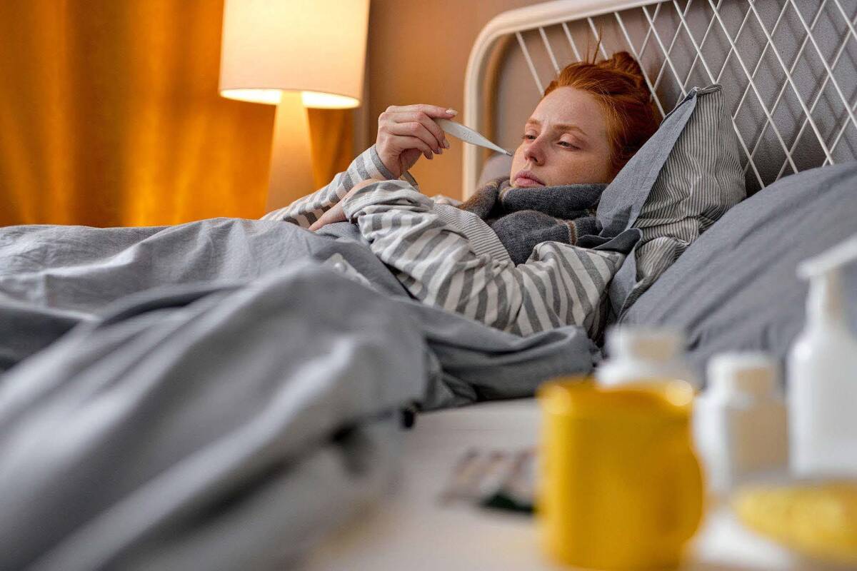 A sick woman checks her temperature with a thermometer while lying in bed, unable to attend her upcoming vacation.