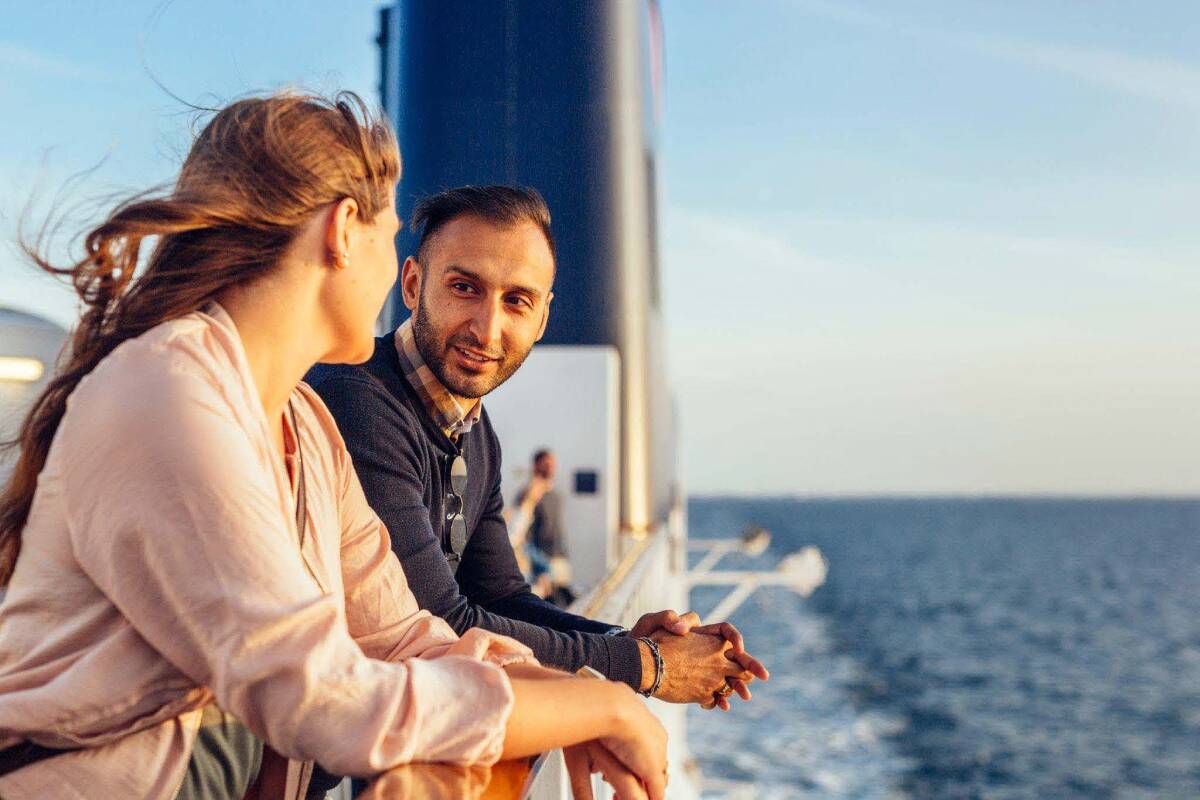 A couple enjoying a conversation while leaning on a Carnival cruise ship railing at sea, highlighting the peace of mind that Aegis cruise travel insurance can bring.