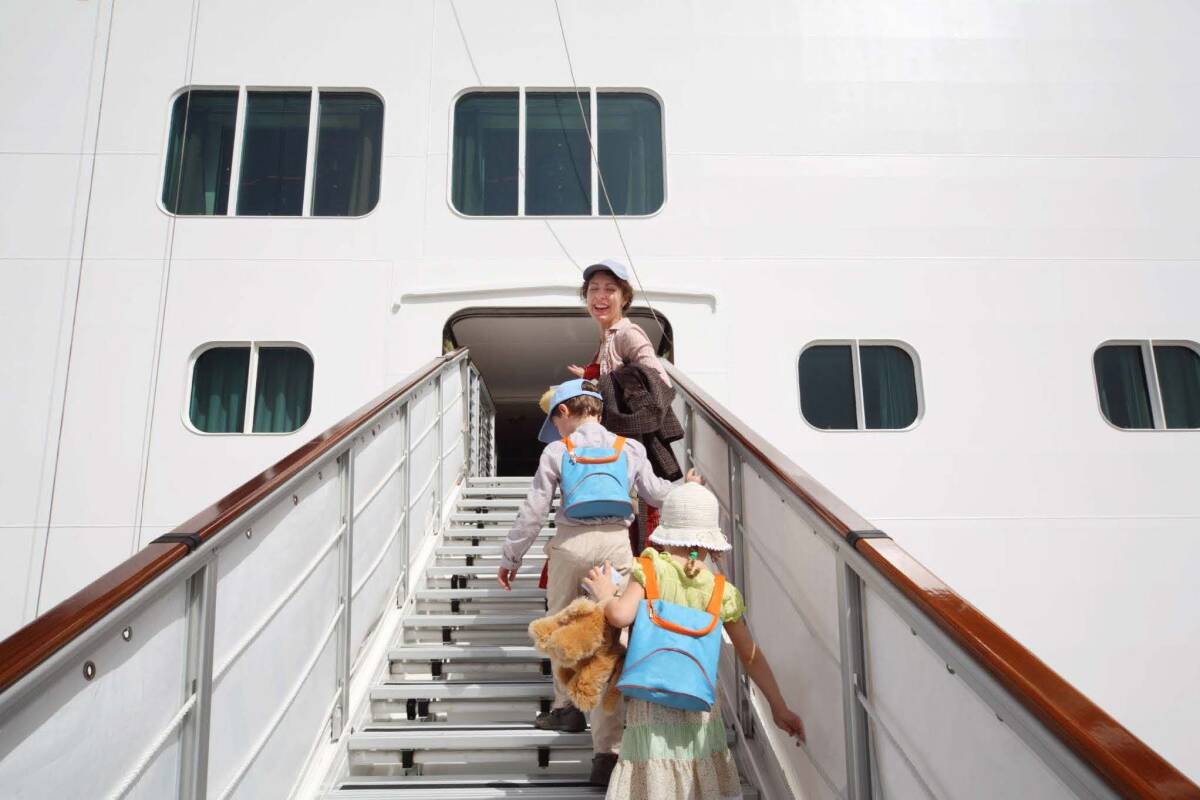 Smiling mother and two children with backpacks boarding a cruise ship via a gangway.