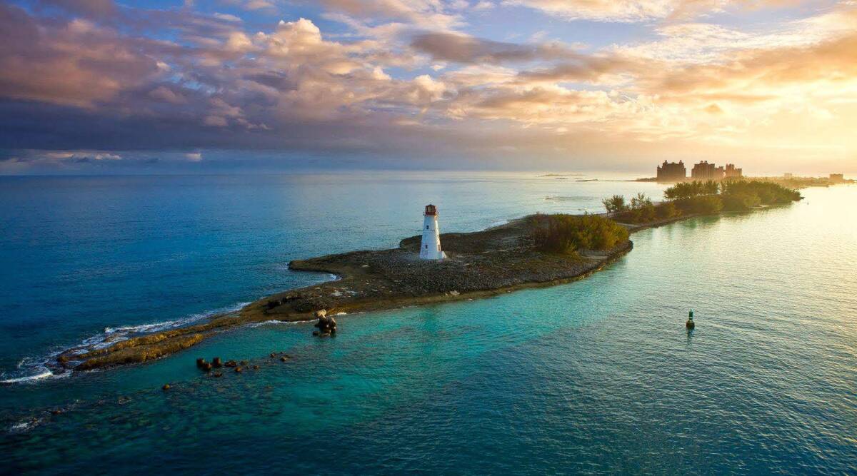 The Bahamas' serene coastline features a lighthouse and     vibrant turquoise seas under a glowing morning sky.